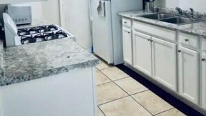 Une cuisine avec des meubles blancs, une cuisinière à gaz, un réfrigérateur et un évier.