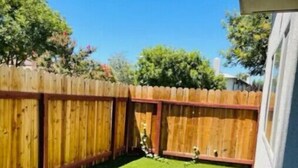 Un jardin avec une clôture en bois, une pelouse bien entretenue et une maison en arrière-plan.