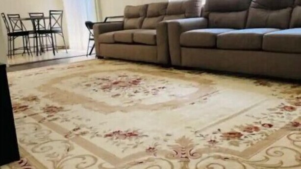 Un salon avec un canapé beige, une table à manger avec des chaises et un tapis à motifs.