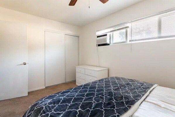 A bedroom with a bed, a dresser, a closet, and a window with blinds.