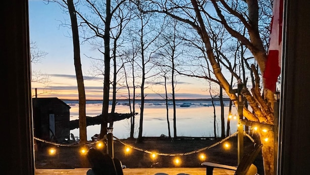 Una terraza con dos sillas Adirondack y una hamaca, con vista a un cuerpo de agua y árboles.