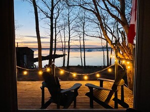 Una terraza con dos sillas Adirondack y una hamaca, con vista a un cuerpo de agua y árboles.