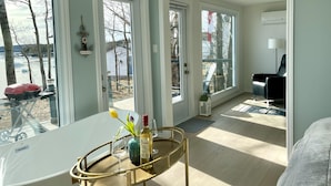 Una habitación moderna con ventanas amplias, una mesa de comedor con un florero y copas de vino, y una silla de cuero negro.