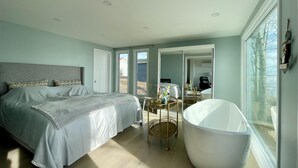 Un dormitorio moderno con una cama grande, una bañera independiente y una mesita con objetos decorativos.