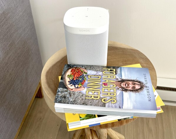 Un altavoz SONOS sobre una mesa de madera con un libro titulado "The Forager's Dinner" de Shawn Ryan.