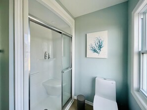 A bathroom with a glass shower enclosure, a toilet, and a framed artwork on the wall.