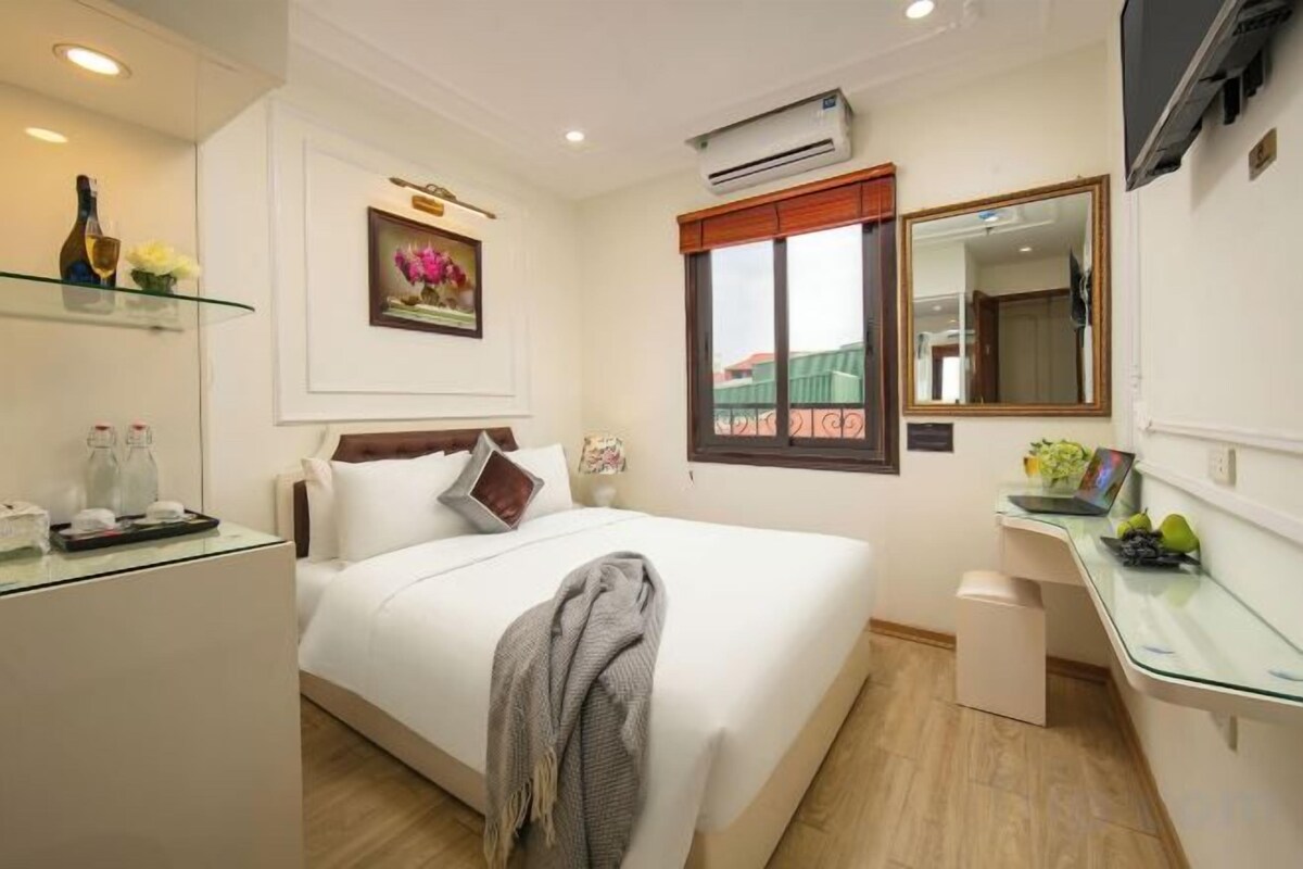 A hotel room with a bed, bedside table, and a desk with a chair.