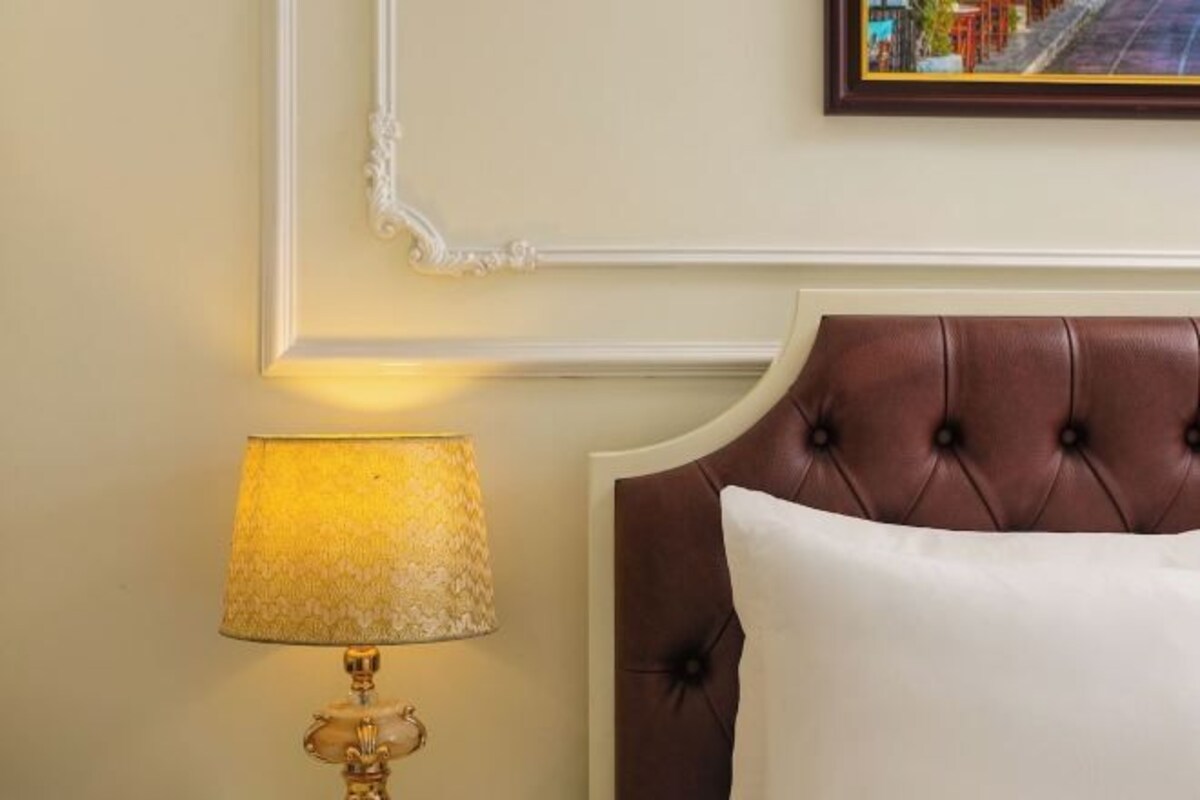 A hotel room with a tufted headboard, a bedside lamp, and a framed picture on the wall.