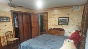 A wooden-paneled bedroom with a bed, a chair, a dresser, and a ceiling fan.