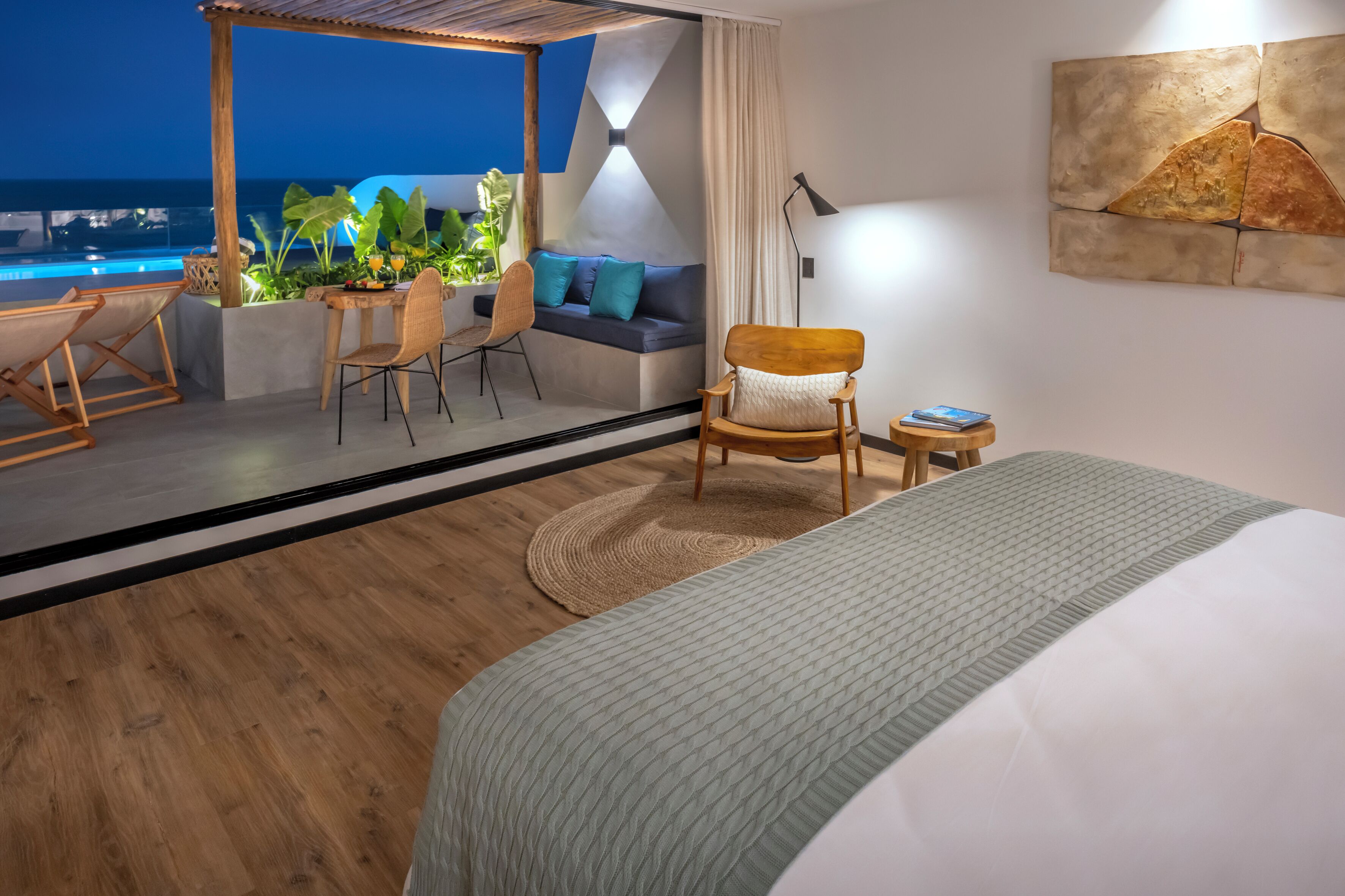 A modern hotel room with a large bed, a seating area with a sofa and chairs, a small table, and a view of the ocean.