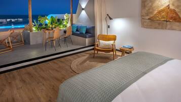 A modern hotel room with a large bed, a seating area with a sofa and chairs, a small table, and a view of the ocean.
