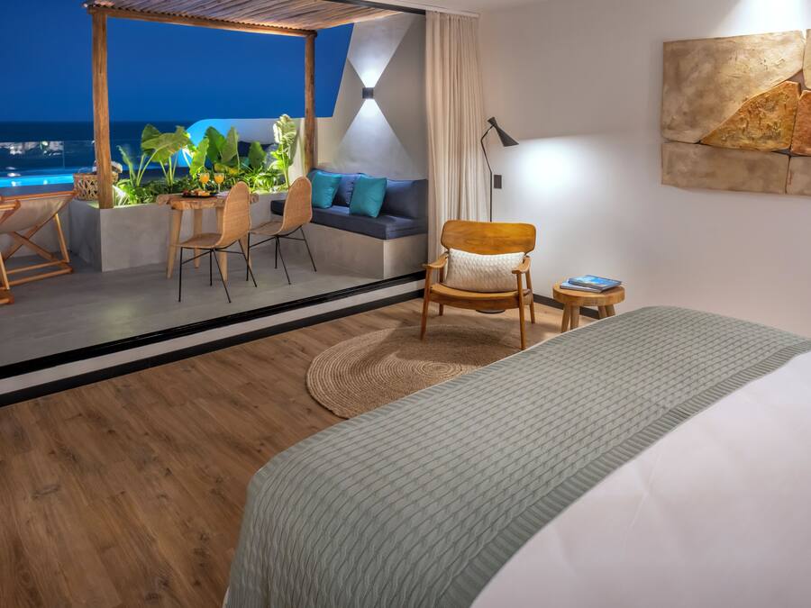 A modern hotel room with a large bed, a seating area with a sofa and chairs, a small table, and a view of the ocean.