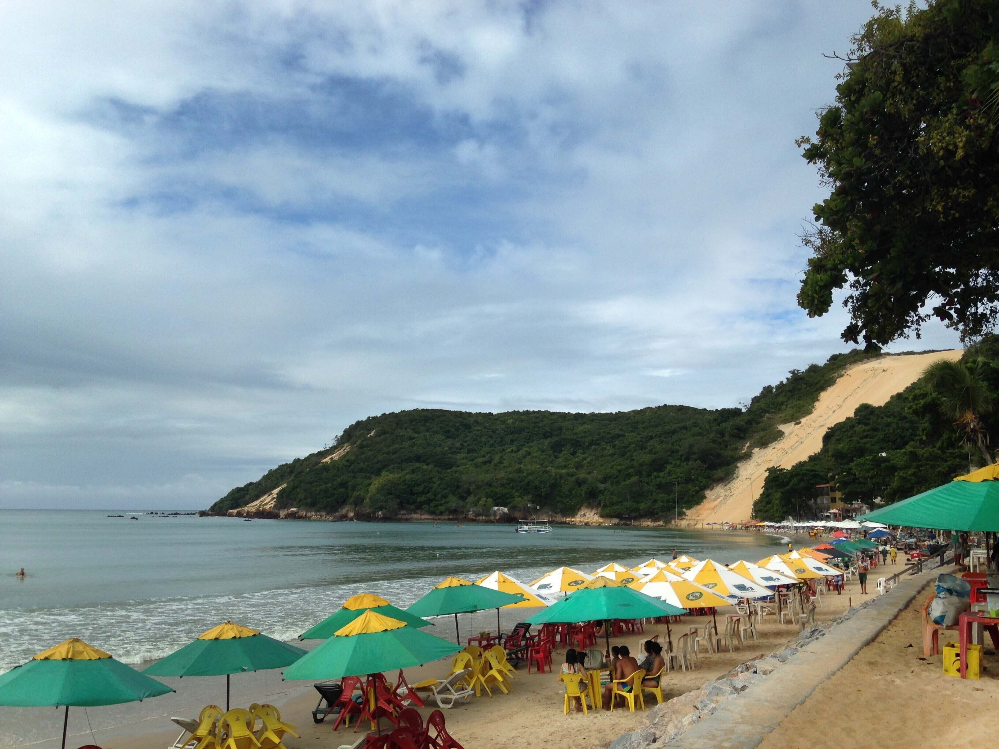 Una playa con hileras de sombrillas y sillas, una orilla arenosa y un paisaje montañoso al fondo.