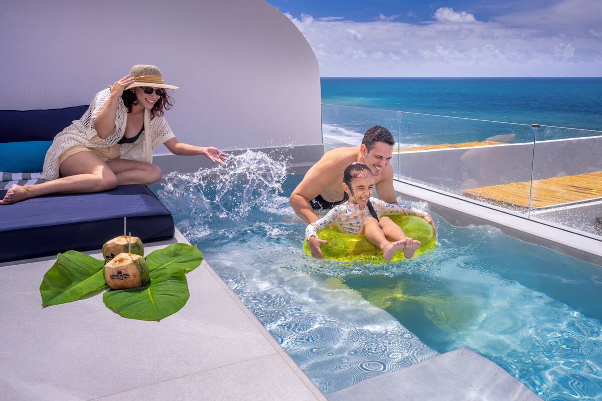 A pool area with a view of the ocean, lounge seating, and a tropical drink setup.