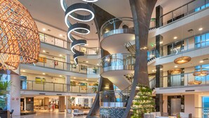 A multi-level atrium with a central spiral staircase, glass railings, and a Christmas tree. - SERHS Experience Suites (Natal)