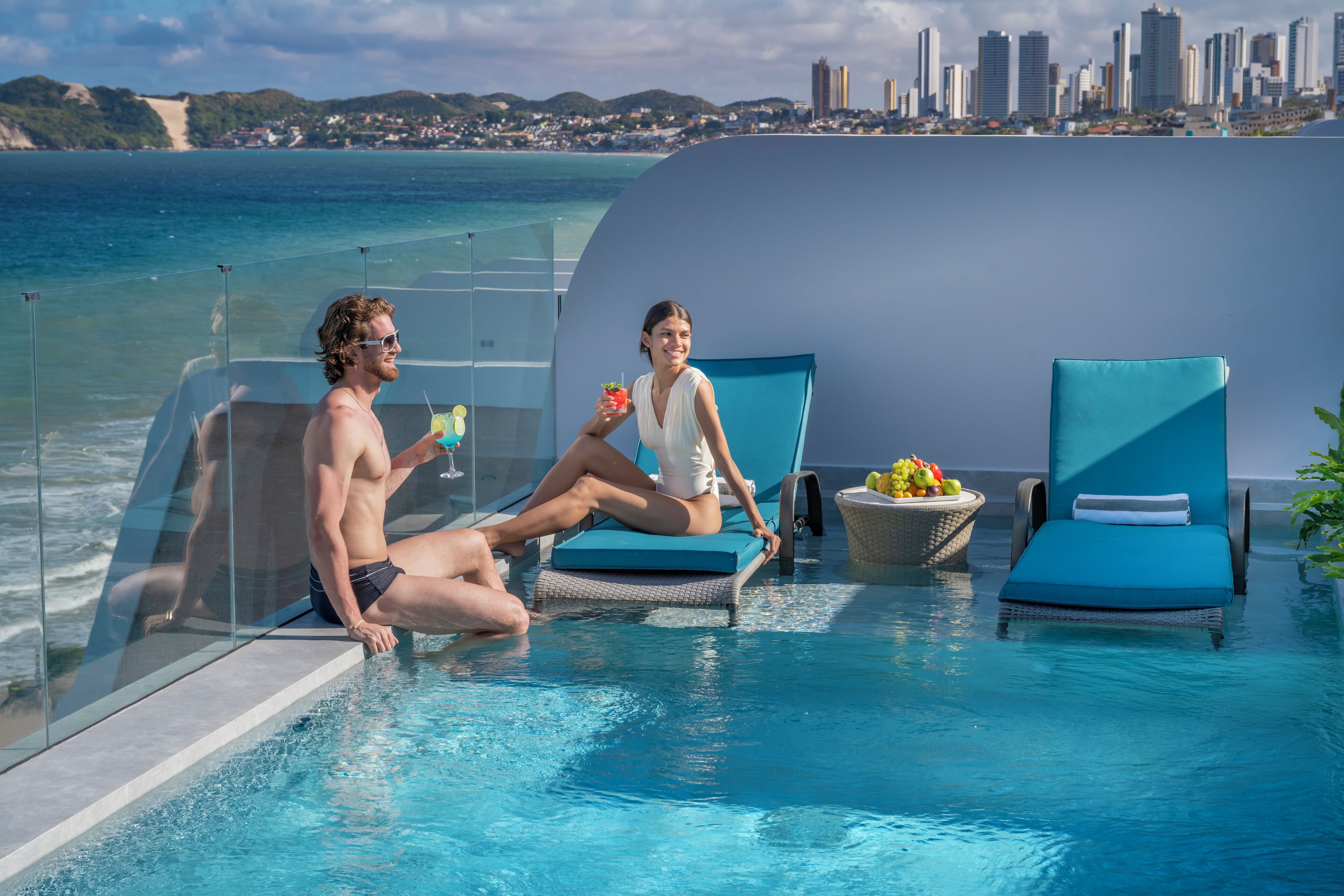 Zona de piscina con sillones de descanso y vista a la ciudad.