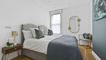Quarto com cama, mesa de cabeceira, luminária e uma cadeira.