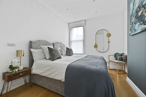 Un dormitorio con cama, mesita de noche, lámpara y una silla.