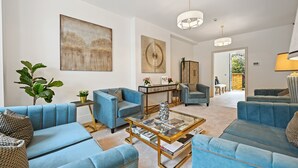 Un salon moderne avec des canapés bleus, une table basse en verre et des œuvres d’art accrochées aux murs.