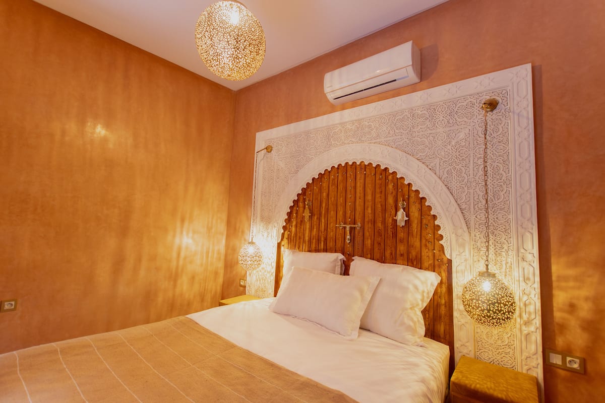 A bedroom with a large bed, an ornate headboard, and two hanging lamps.