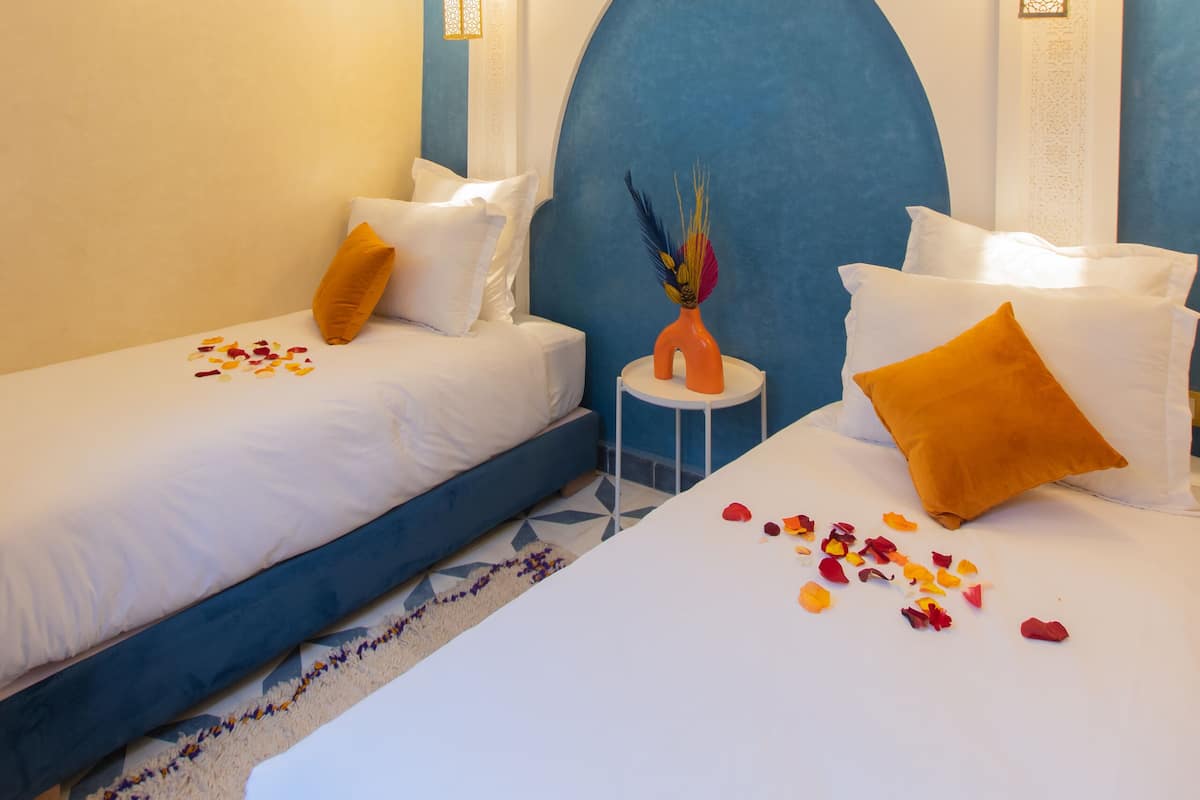 A hotel room with two beds, a decorative ceiling light, an air conditioning unit, and a small table with a vase.