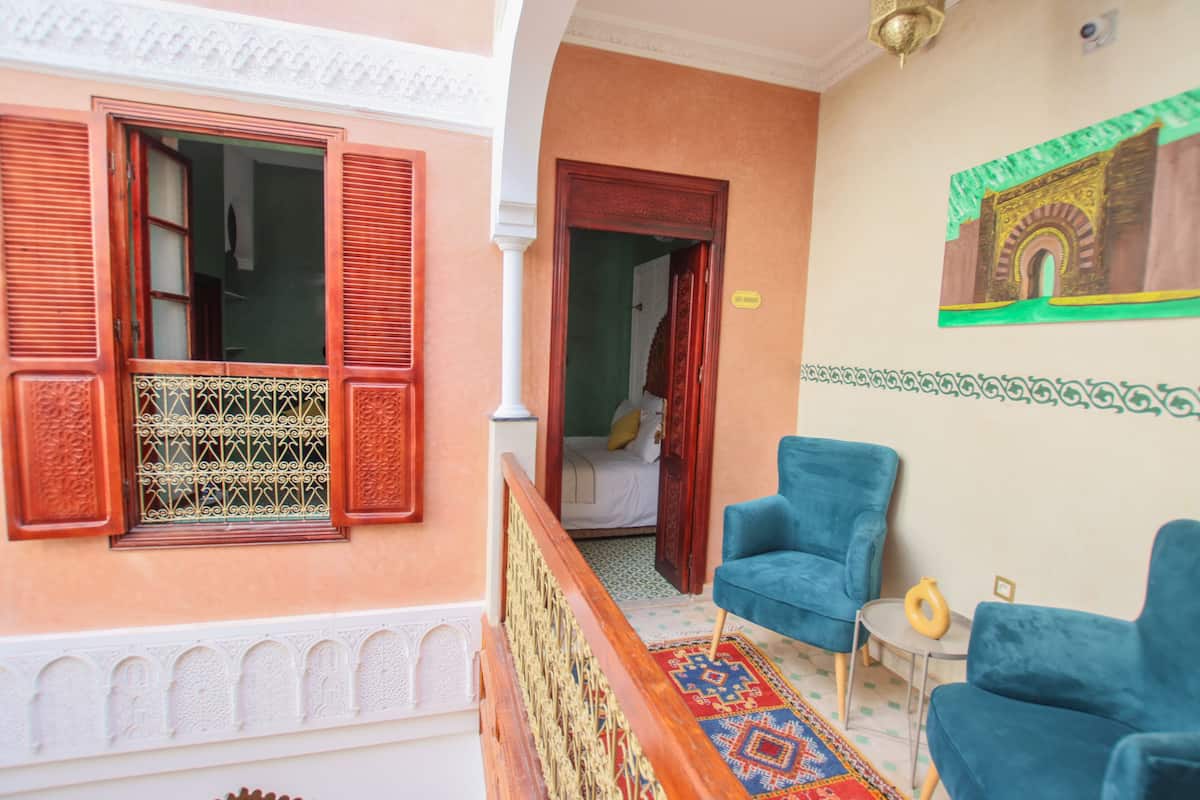 A room with a balcony, a patterned rug, and two blue armchairs.