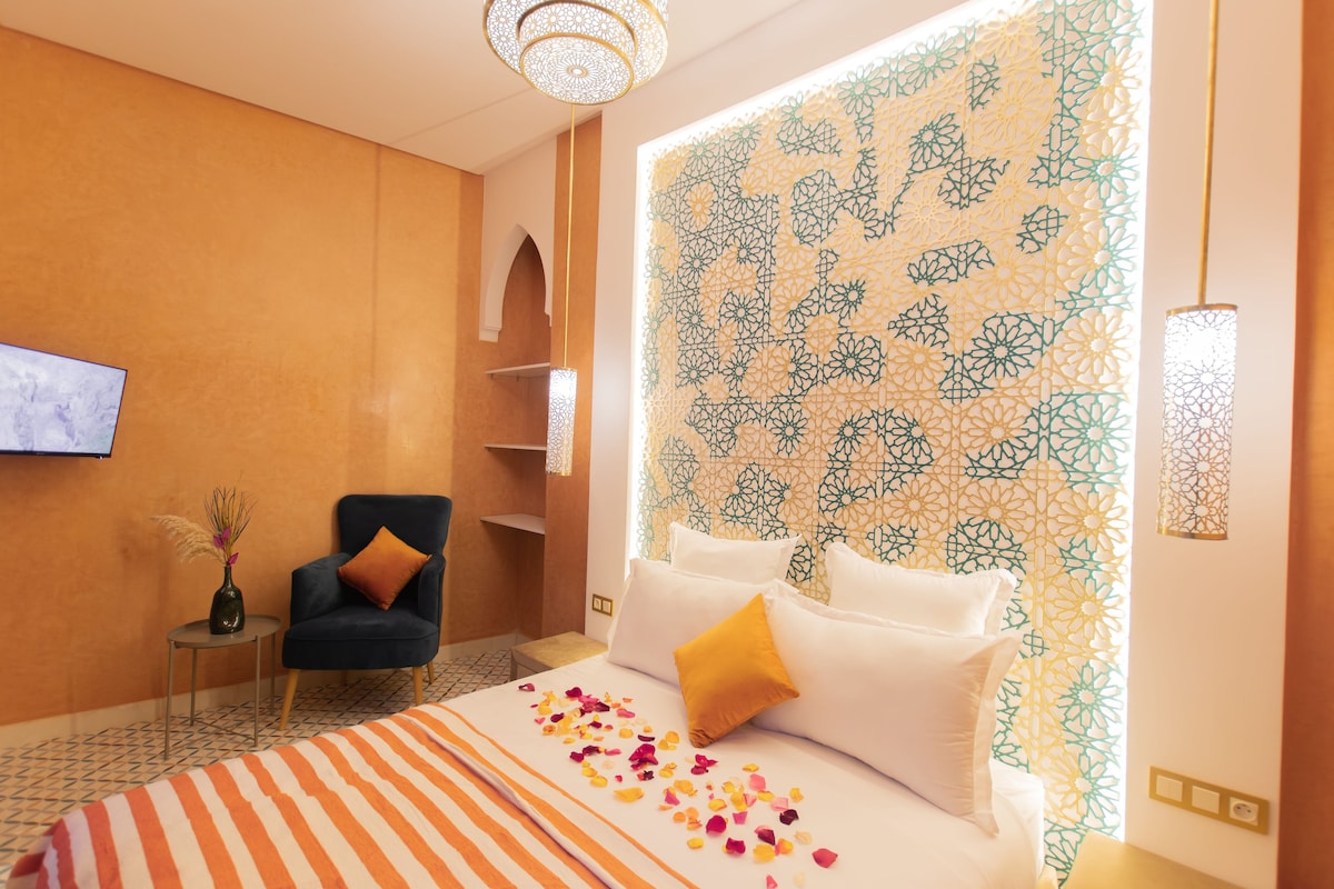 A hotel room with a bed, a chair, a TV, and a patterned wall.