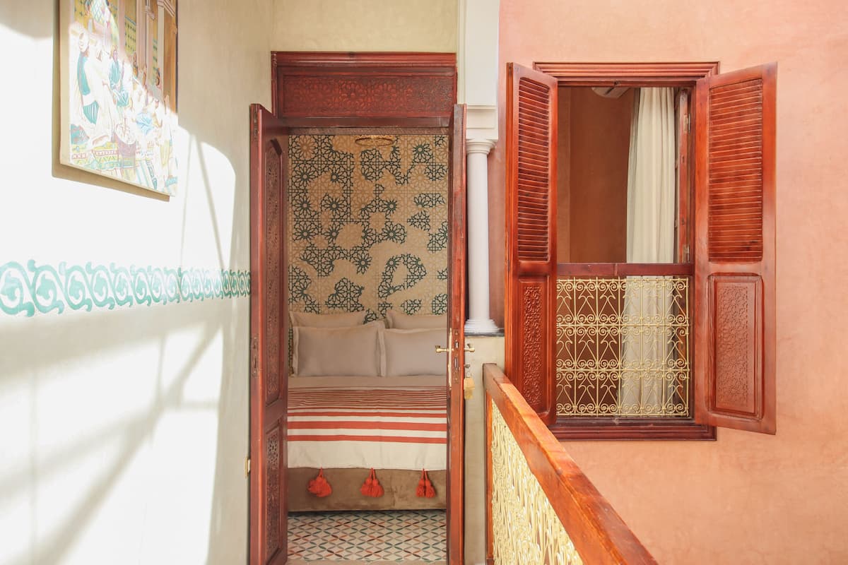 A narrow hallway with a bed, a window with a metal grille, and a wall with a patterned design.