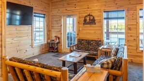 A log cabin interior with a sofa, chairs, a table, and a TV mounted on the wall. - Waterfront Northwoods Bunkhouse 19B (Houghton)