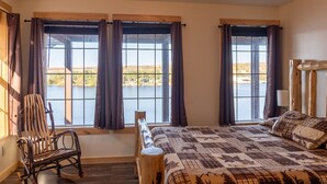 A bedroom with a large bed, a chair, and a view of a lake through windows. - Waterfront Northwoods Bunkhouse 19B (Houghton)