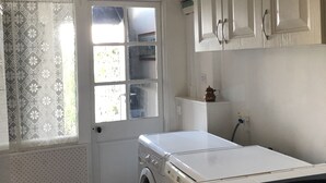 A compact kitchen with a washing machine, a sink, and a window with patterned curtains. - Maison Ancienne Avec son Jardin Privatif (Le Havre)