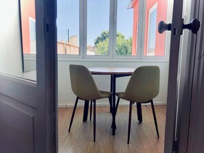A room with a wooden floor, two chairs, a small table, and a window with a view of a fence and greenery.