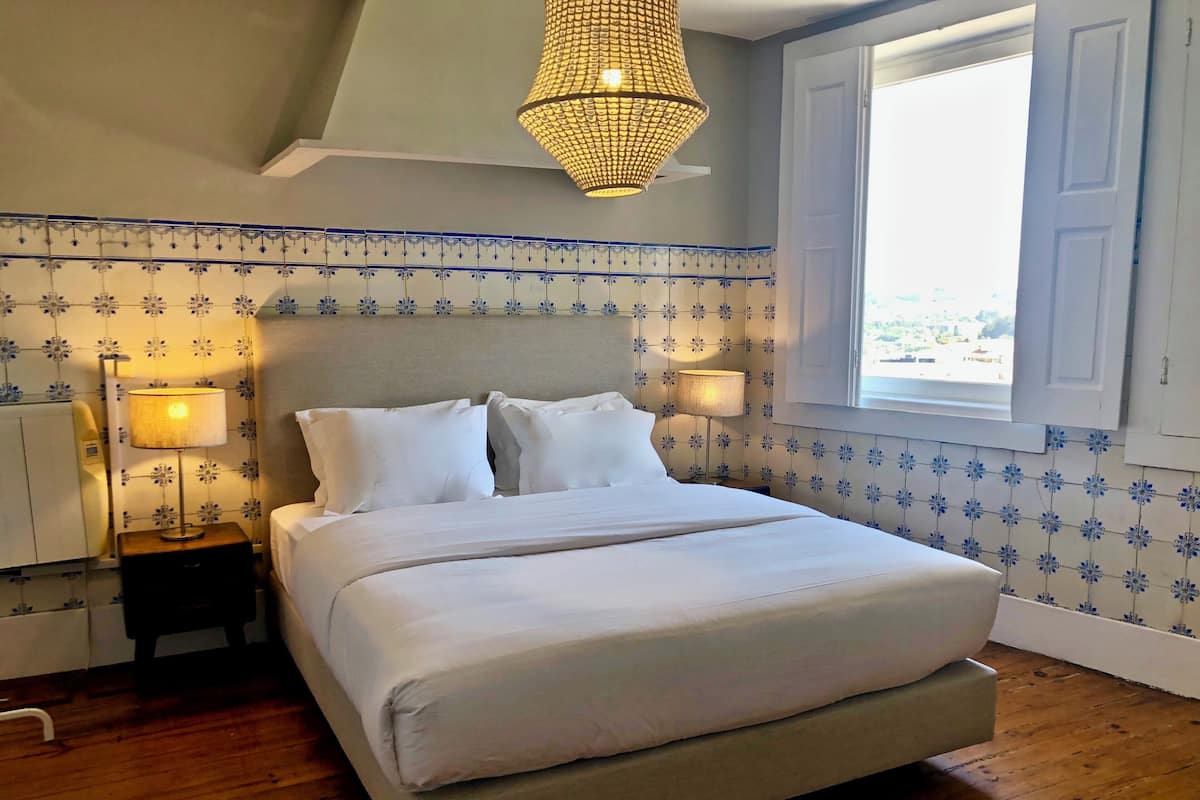 A bedroom with a bed, bedside lamps, a chandelier, and a window.