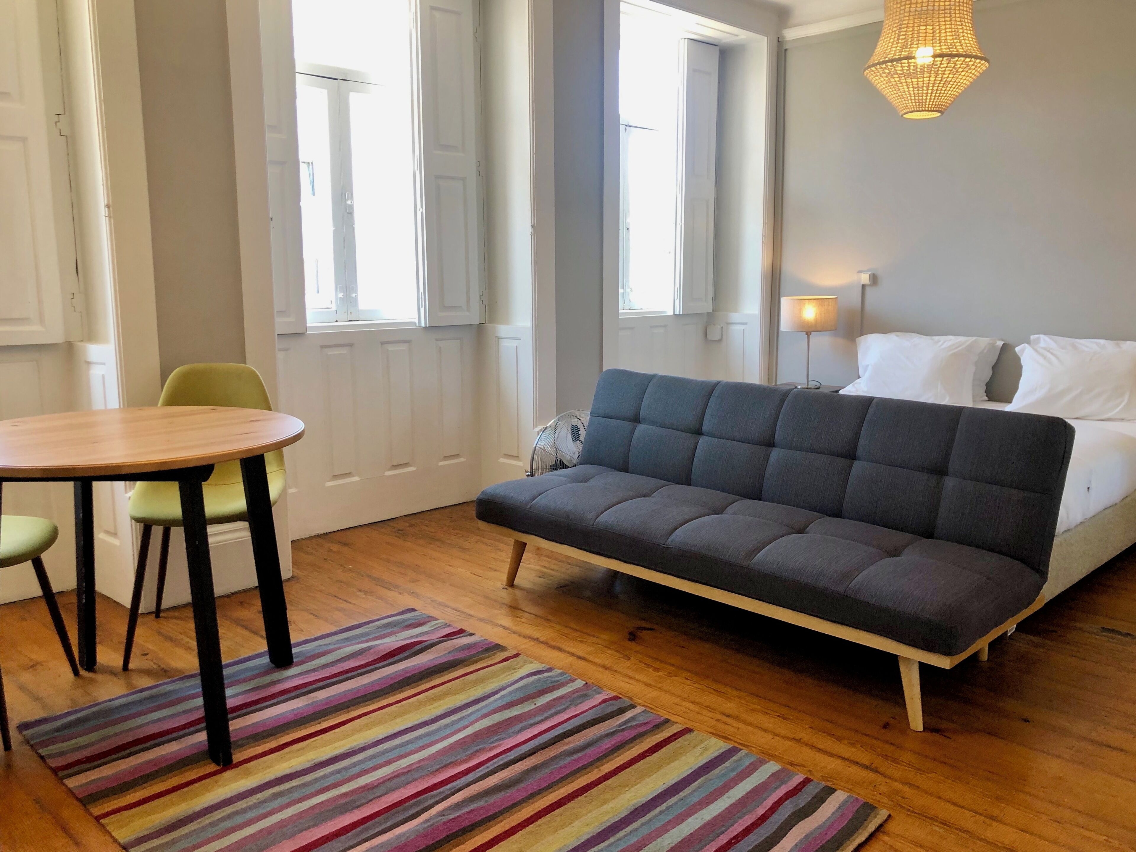 Une pièce comprenant un lit, un canapé, une table à manger avec des chaises et un tapis rayé aux couleurs vives.