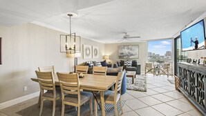 A spacious living area with a dining table and chairs, a sofa, and a balcony with a city view. - Mainsail 362 - Gulf Front Condo, Community Pool, Hot Tub, Free Beach Service! (Miramar Beach)