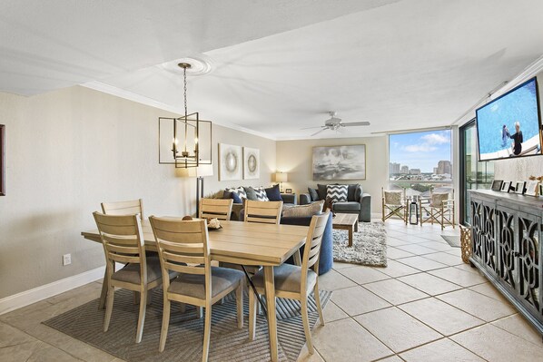 A spacious living area with a dining table and chairs, a sofa, and a balcony with a city view. - Mainsail 362 - Gulf Front Condo, Community Pool, Hot Tub, Free Beach Service! (Miramar Beach)
