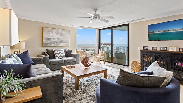 A spacious living room with a grey sofa, a wooden coffee table, and a view of the ocean through large sliding glass doors. - Mainsail 362 - Gulf Front Condo, Community Pool, Hot Tub, Free Beach Service! (Miramar Beach)