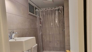 A bathroom with a shower, toilet, sink, and a window above the shower.