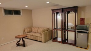 A room with a beige sofa, a small wooden table, a cabinet with a mirror, and a microwave.