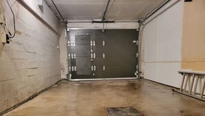 A clean, empty hallway with a closed garage door, concrete floor, and a metal handrail on the right.