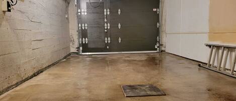 A clean, empty hallway with a closed garage door, concrete floor, and a metal handrail on the right.
