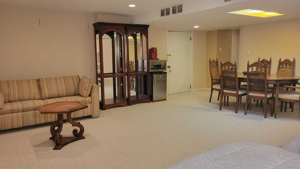 A living room with a sofa, a coffee table, a dining table with chairs, and a kitchen area with a refrigerator and microwave.