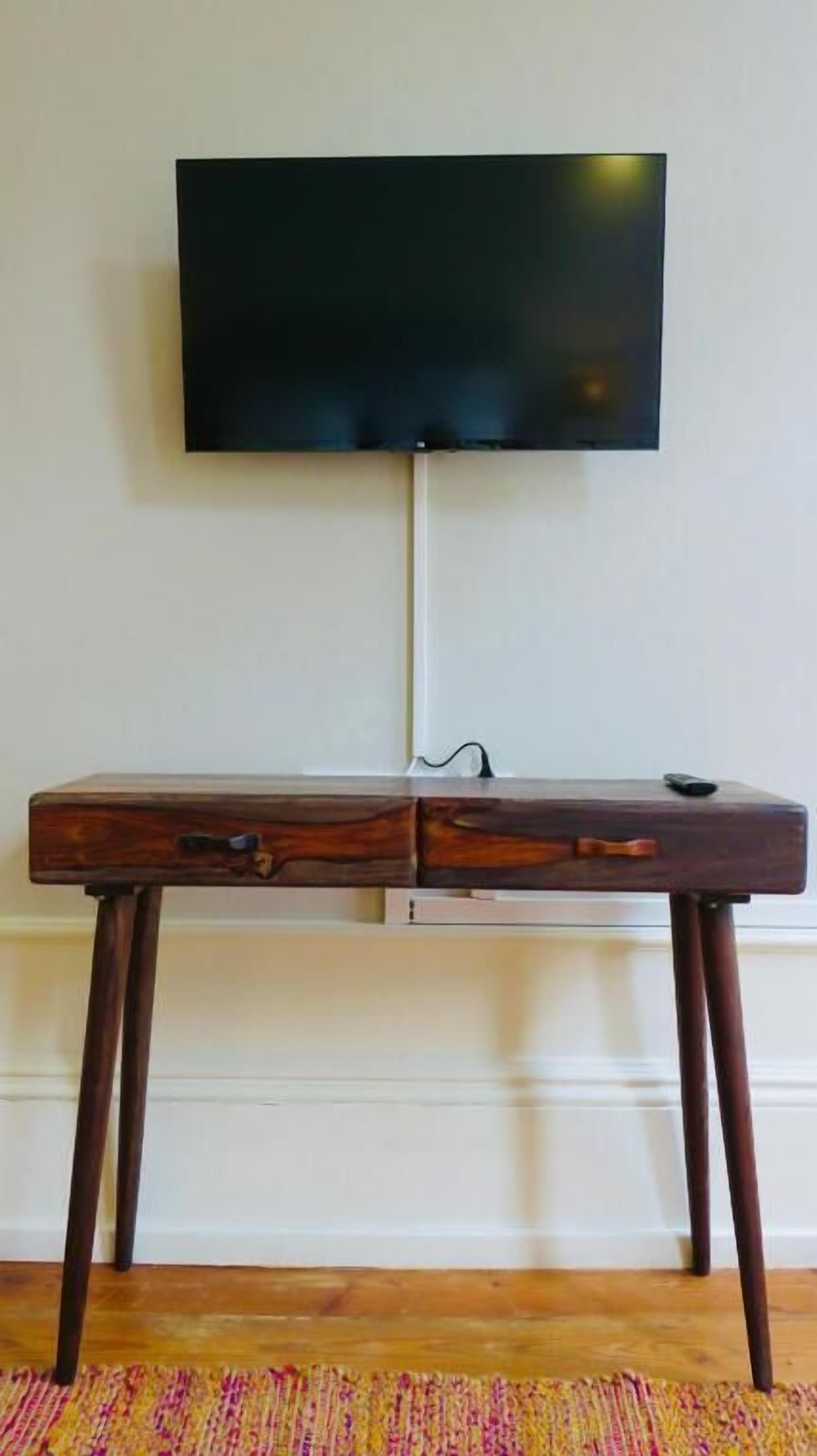 A wooden desk with drawers and a flat-screen TV mounted on the wall above it.