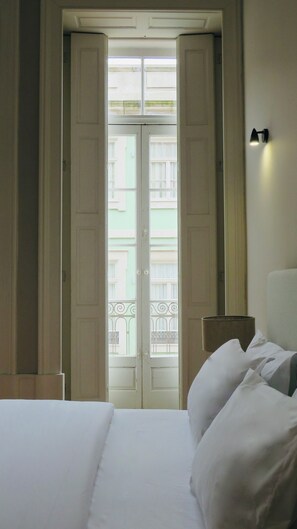 A hotel room with a bed, a nightstand, a lamp, and a view of a building through a door. - Porto República Ribeira (Porto)