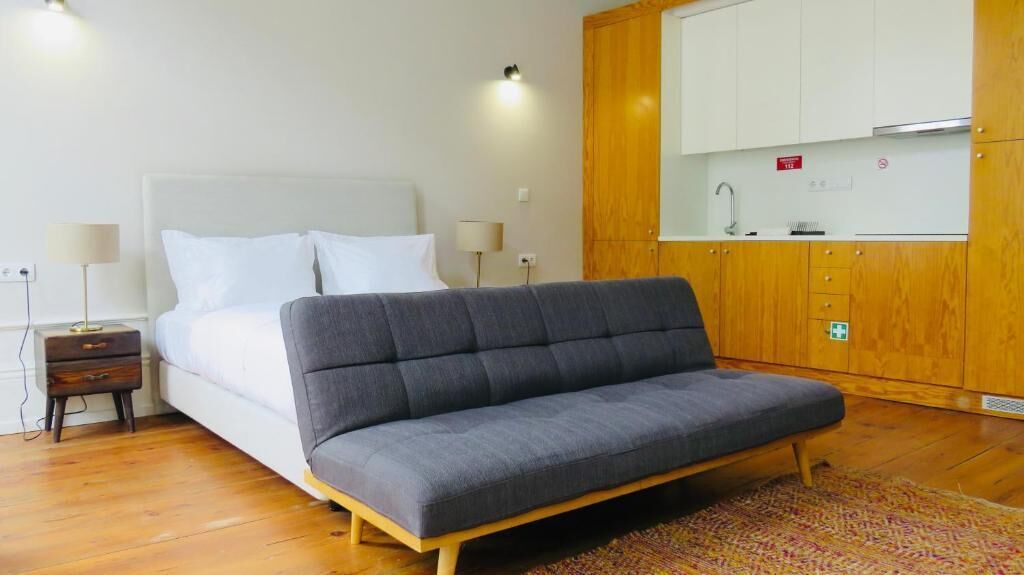 Un dormitorio con cama, mesitas de noche, sofá, armario de madera y zona de kitchenette.