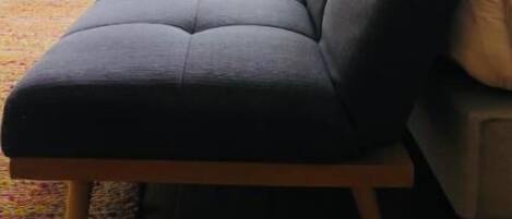 A grey sofa with wooden legs in a room with large windows and white curtains.