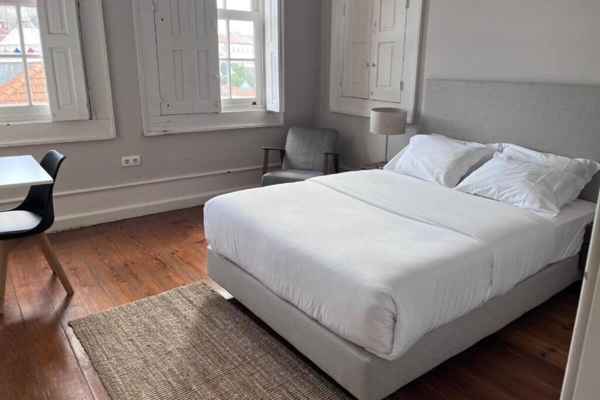 A bedroom with a large bed, a chair, a desk, and a lamp.