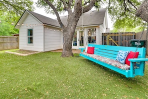 Un jardin avec une balançoire turquoise, une maison blanche et une clôture en bois.