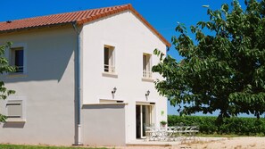 Stylish two-story building with a balcony, door, and window, set amidst a landscaped area with a tree and hedge.