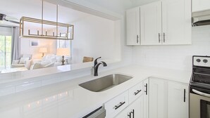 A modern kitchen with white cabinetry, a stainless steel sink, and a built-in oven. - Grayton Beach Villas 101 - Scenic 30A, Steps to the Sand, Walk to Red Bar! (Grayton Beach)